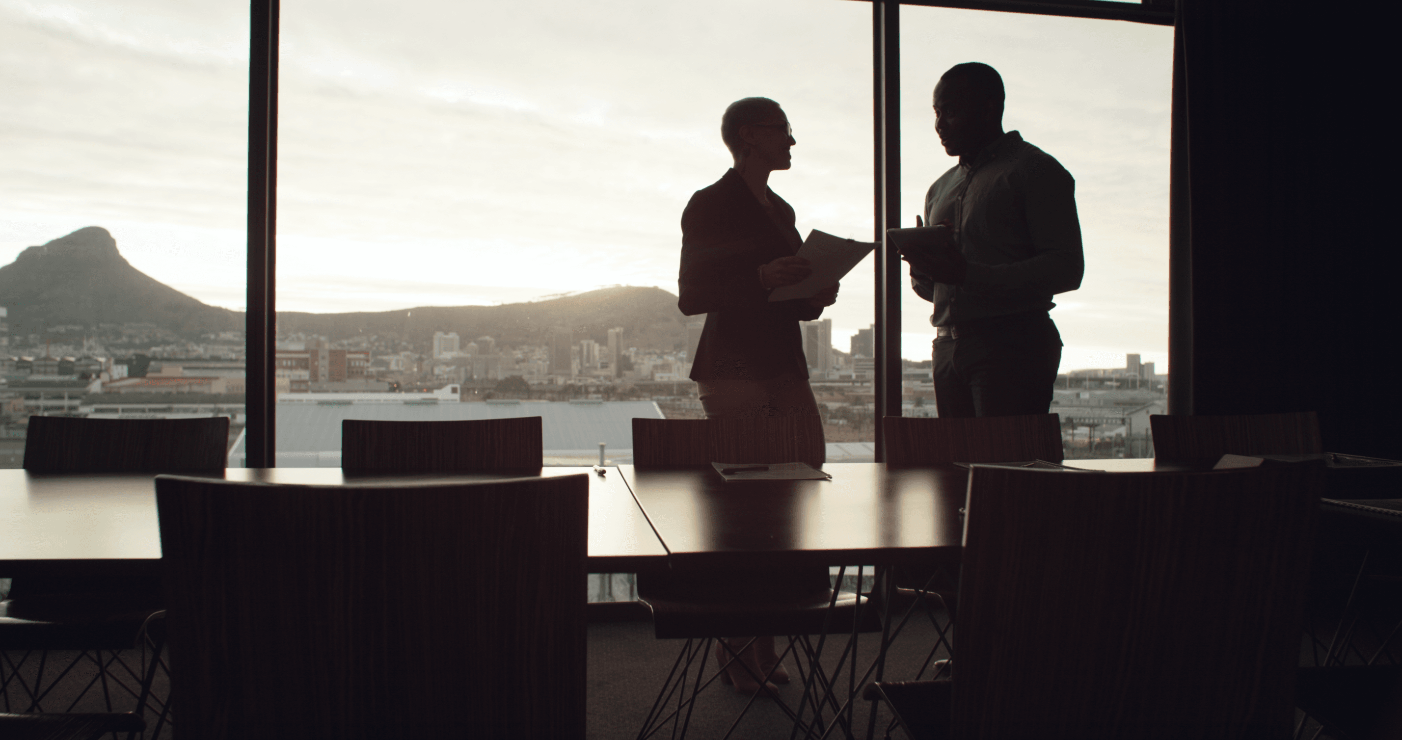Abendsonne beleuchtet einen Meetingraum, in dem man die Umrisse zweier Geschäftsmänner im Gespräch sieht.